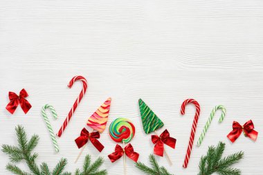 Noel tatlıları çeşitli üst manzara, yeşil köknar dalları, beyaz arka planda tahta oyuncaklar, düz bir zemin. Parlak yeni yıl şekeri ve lolipopları.