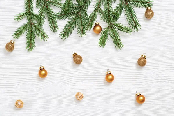 メタリックゴールデンおもちゃ 白い木製のテーブルの上に小さな明るいボール 自然の緑のモミの木の枝が落ちる 冬休みのコンセプト 平置きだ トップ表示 — ストック写真
