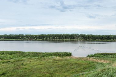 Irtysh nehrinin kolları ve parlak mavi gökyüzü ile doğa manzarası, şişme tekne suyun üzerinde yüzüyor. Omsk bölgesindeki nehir kıyısına sahip doğal arka plan, Rusya.