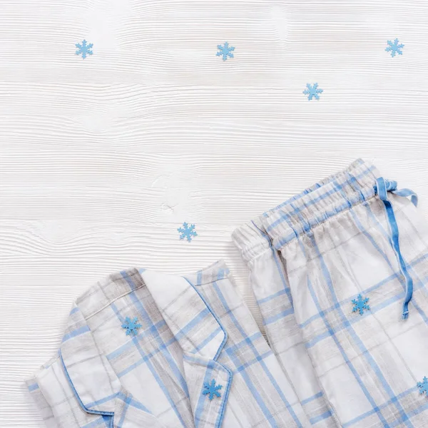 White cotton pajamas with blue checks or stripes, on white wooden background with copy space. Nightwear for sleeping with snowflakes for winter time. Top view