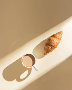 Lezzetli kruvasan ve bej arka planda sütlü kahve fotokopi alanı ve güneş ışığıyla. Güneşli yaz gününde kahvaltı. Üst manzara, parlak ışık.