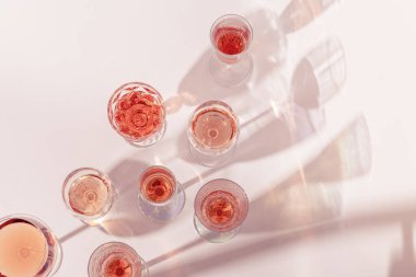 Kristal bardaklarda gül şarabı, gül şampanyası güneş ışığı gölgeli şampanya. Alkolik yaz içkisi üst görünüm, şarapçılık konsepti.