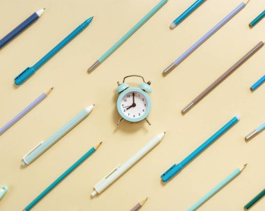 Alarm saati sabah 8 oktav gösteriyor, okula gitme zamanı. Bej arka planda mavi kalem ve kalemlerden saat ve geometrik desenli yaratıcı Düz yatıyordu.