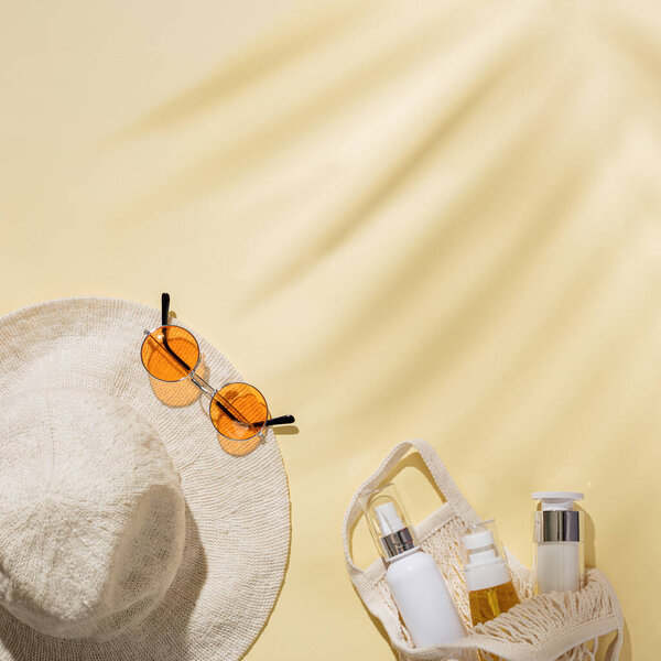 Summer minimal background with sun hat, colored sunglasses and cosmetic product in mesh bag on sandy color background. Summertime concept pastel colored aesthetic photo.
