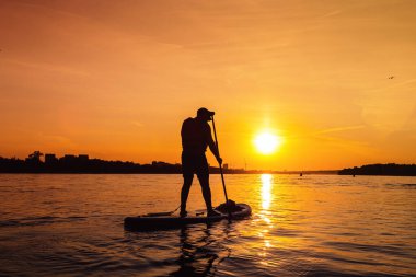 Gün batımında siluet kürek sörfçüsü. Şehir nehrinde kayıkla gezen adam. Açık hava aktiviteleri, yerel turizm kavramı.