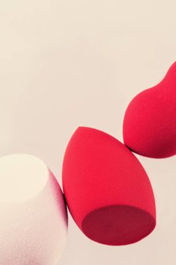 Kırmızı ve pembe kozmetik güzellik süngerleri bej arka planda fotokopi alanı ile kapanır. Ton kremi, fondöten ve kapatıcı için makyaj şişesi. Üst görünüm, makro.