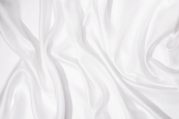 Cloth texture background white colors. Bright satin fabric with creases on fabric close up. Hard light and top view.