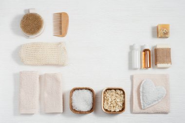 Doğal malzemeden banyo aksesuarları, banyo için sıfır atık seti, pamuk havlular, jel ve şampuanlı küçük şişeler, sabun, deniz tuzu, beyaz ahşap masadaki bez ve fotokopi alanı..