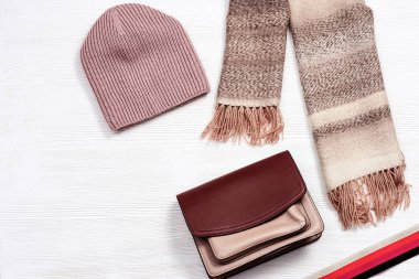 Sonbahar dairesi sıcak yün atkısı, örgü şapkası ve küçük kadın deri çantasıyla yatıyordu. Beyaz ahşap masada sonbahar kıyafetleri. Üst görünüm.