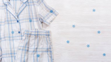 Beyaz pamuklu pijamalar, mavi çekli ya da çizgili, beyaz ahşap arka planda fotokopi alanı olan. Kış zamanı kar taneleriyle yatmak için gecelik. Üst görünüm pankartı.