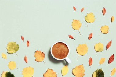 Sütlü kahve ve pastel yeşil kağıtta kırmızı sarı sonbahar yaprakları. Sonbahar, sonbahar kompozisyonu, düz konum, üst görünüm, kopyalama alanı