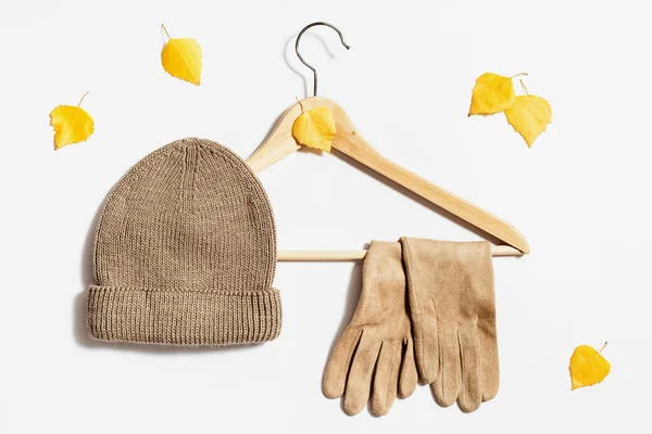 米色的针织帽子和绒毛手套挂在白色背景的衣架上 装饰着秋天黄色的叶子 时尚秋装的概念 温暖的衣服为寒冷的天气 为妇女和女孩 顶部视图 — 图库照片