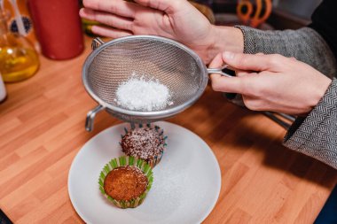 Keklerin üzerine şeker dökmek için süzgeç kullanan eller. Mutfakta tatlılar hazırlanıyor..