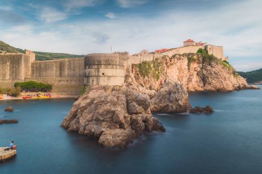 Eski Dubrovnik kasabasının güneşli bir öğleden sonra manzarası ve Hırvatistan 'daki Adriyatik Denizi' nin ön planında bir balıkçıyla kent duvarları.