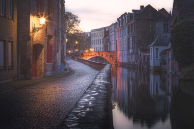 Belçika 'nın Bruges kentindeki sakin bir akşam kanalında kaldırım kenarında ayak izleri var..