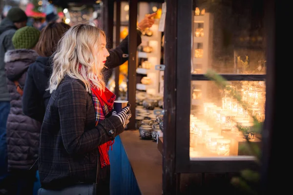 スコットランドのエディンバラ クリスマスマーケットでホットドリンクを飲みながら 若いブロンドの女性が華やかなクリスマスランタンを閲覧します — ストック写真