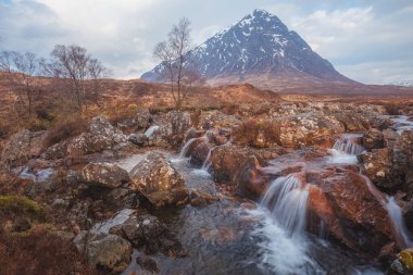 İskoçya 'daki Glencoe' daki Buachaille Etiv Mor ve River Coupall şelalesinin dramatik manzarası.