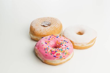 Sade beyaz bir zemin ve arka planda izole edilmiş üç taze, renkli halka çöreği..