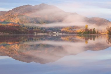 İskoçya 'daki İskoçya Highlands' taki Trossachs Ulusal Parkı 'nda Loch Lomond Gölü' ndeki sabah sisi ile sakin bir dağ manzarası yansıması..