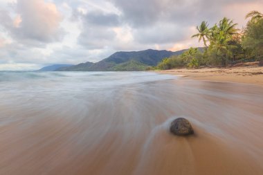 A lone rock on an idyllic, tropical sandy Thala Beach near Oak Beach at sunrise or sunset outside Port Douglas and the Daintree in Queensland, Australia.