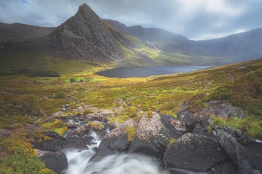 Kuzey Galler 'deki Snowdonia Ulusal Parkı' ndaki Tryfan Tepesi ve Llyn Ogwen ve Vadisi 'nden yayılan karamsar, dramatik dağ akıntısı ve ışık ışınları manzarası.