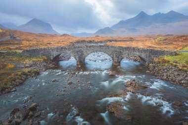 A dramatic landscape view of the old Roman stone bridge at Sligachan River and Black Cuillin mountains on the Isle of Skye, Scottish Highlands, Scotland. clipart