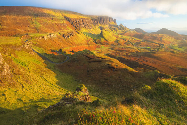 Vibrant golden light at sunset or sunrise over colourful landscape view of the rugged, otherworldly terrain of the Quiraing on the Isle of Skye, Scotland.
