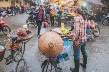 Yerel bir Vietnamlı sokak satıcısı Hanoi 'nin hareketli caddelerinde yağmurlu bir günde bisikletinin arkasından meyve satıyor..