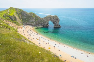 İngiltere 'nin Dorset kentindeki Jurassic Sahili' nde güneşli bir yaz gününde ikonik deniz kemeri Durdle Door 'daki plajda turistler.