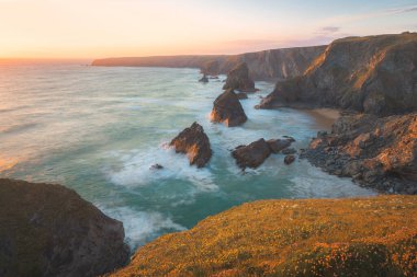 Kuzey Conrwall, İngiltere 'deki Carnewas ve Bedruthan Steps kaya oluşumlarında gün batımı veya gün doğumuyla birlikte dramatik deniz manzarası..