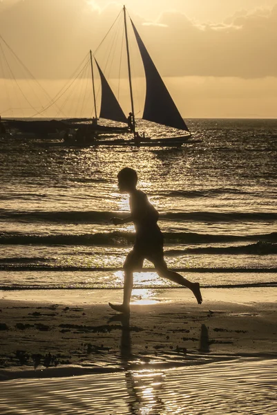 Силует хлопчика, що біжить на дивовижному помаранчевому заході сонця з човнами — стокове фото