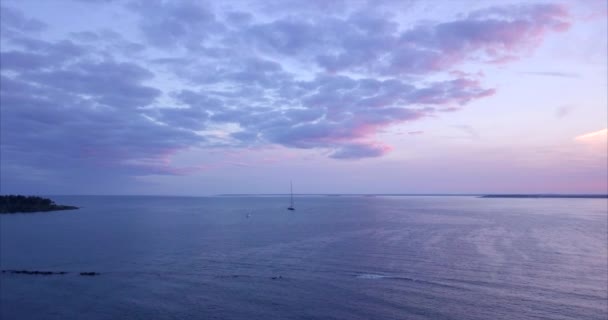 メイン州の海岸線からの劇的なピンクと紫の夕日の間に1隻の帆船で穏やかな港を飛び回る空中ショット — ストック動画