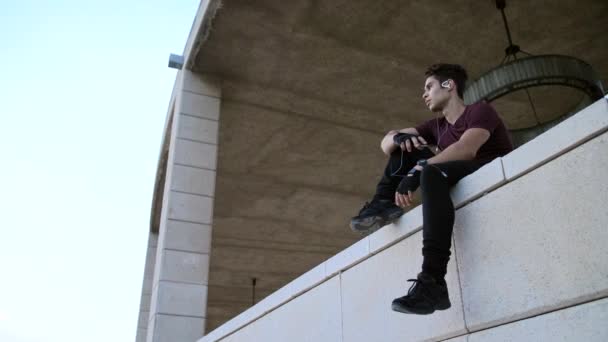 穿着运动服的有魅力的高个子男子爬上具有城市背景的高墙 用手机听音乐 — 图库视频影像