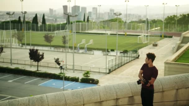 スポーツウェアの魅力的な背の高い男は 異なる演習を行うと 足で温暖化し 実行していると記念碑的な都市の背景を歩く — ストック動画