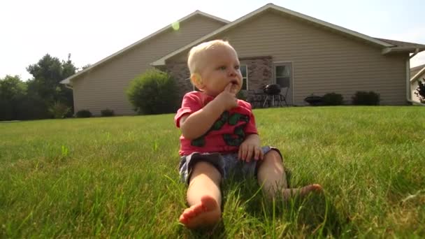 Ένα Μωρό Κάθεται Στο Γρασίδι Ρουφώντας Δάχτυλό Του Και Χαμογελώντας — Αρχείο Βίντεο