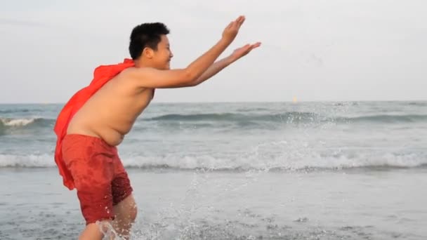 ビーチで赤いフードスプラッシュ水で幸せな脂肪の男の子 スローモーション — ストック動画