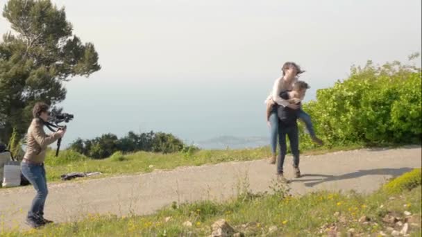 Professional cameraman walking backwards while using a camera and gimbal stabilizer to film a fun happy caucasian couple piggyback riding outdoors in nature.