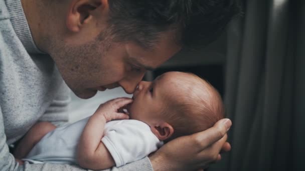 誇り高い父は 彼らが見つめ合うように彼の赤ちゃんの男の子を抱きしめます お父さんは腕と笑顔で新生児の鼻をこすります スローモーション — ストック動画
