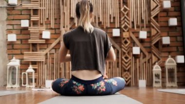 Genç bir yoga öğrencisi bir duvarın önünde rahatlatıcı meditasyon egzersizi yapıyor. Arkadan vurulmuş, el kamerasıyla..