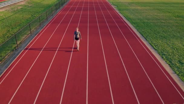 ランニングトラック上のティーン女の子選手は 空中カメラの下に向かって暖まる — ストック動画