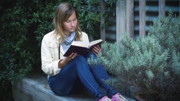 迷人的少女在院子里的植物中看书 — 图库视频影像