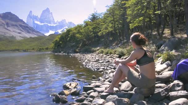 ラグナ カルピの湖のそばに座っている若い女性は アルゼンチンのパタゴニアにあるフィッツ ロイを見ています アルゼンチンのエルチャルテン近くでフィッツ ロイをトレッキング 旅と冒険のコンセプト — ストック動画