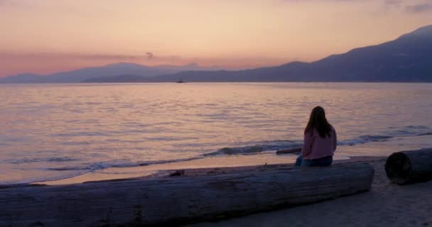 在美丽的加拿大不列颠哥伦比亚省 一位年轻女子坐在一处静谧的海滩上 凝视着美丽的落日 — 图库视频影像