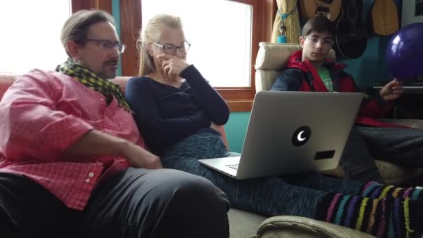Felnőtt férfi és nő beszélni tini fiú laptop egy nappaliban.