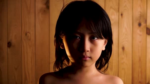戏剧化的灯光照射着年轻的亚洲男孩 赤身露体地看着木制背景的相机 — 图库视频影像