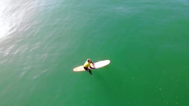 ハンティントンビーチで太平洋の波をキャッチするサーファーザンダー アデルソンパドル4Kの空中ドローンから黄色のウェットスーツを着てサーフィン大会で — ストック動画