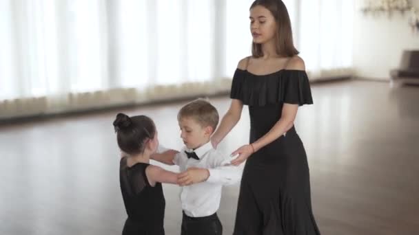 Kézzel fogható felvétel egy gyönyörű fiatal tánctanárról, aki egy helyes fiút és egy lányt tanít táncolni egy táncórán.