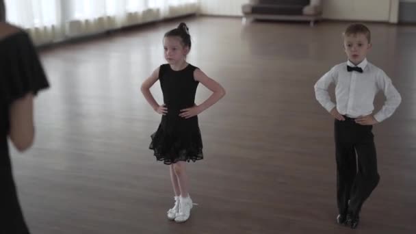 Kézzel fogható felvétel egy gyönyörű fiatal tánctanárról, aki egy helyes fiút és egy lányt tanít táncolni egy táncórán.