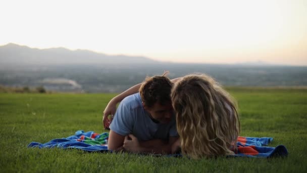拍可爱的男朋友和女朋友躺在毛毯上在草地上野餐 这对夫妇在亲吻 嬉闹地扭打着 — 图库视频影像
