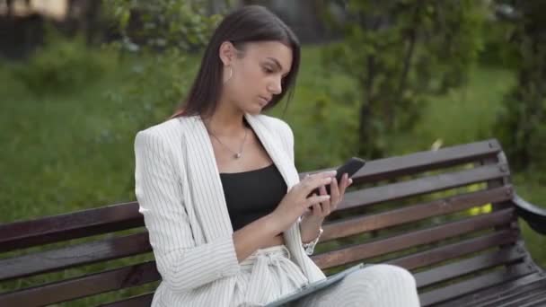 Joven Mujer Negocios Comprueba Teléfono Inteligente Sentado Banco Parque — Vídeo de stock